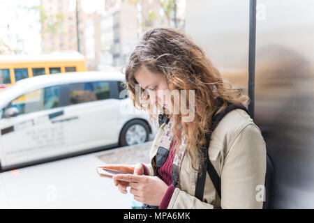 Nahaufnahme der jungen Frau Tourist in Jacke steht die Gebäudewand in NYC New York City urban belebten Straße, Autos im Verkehr mit Handy zu finden Stockfoto