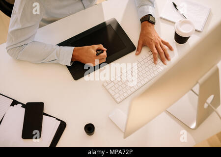 Blick von oben auf ein Mann schreiben auf Digitalisierer mit dem Computer vor. Mann bei der Arbeit am Computer mit einer Tasse Kaffee auf dem Tisch. Stockfoto