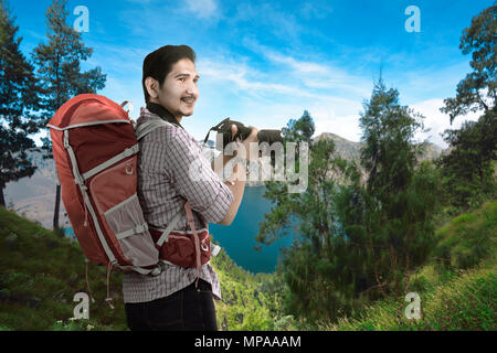 Gerne asiatische Reisende Mann mit Kamera und Rucksack mit Landschaft Hintergrund Stockfoto