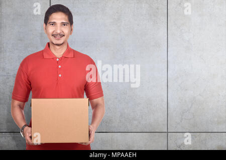 Jungen asiatischen Delivery Man holding Kartons über graue Wand Hintergrund Stockfoto