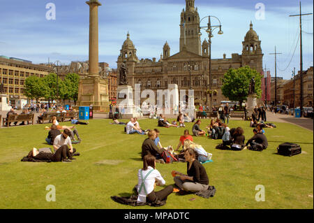 Einheimische und Touristen mit Büroangestellten auf ihr Mittagessen genießen Sie sitzen auf dem Gras auf dem George Square, Glasgow, Großbritannien Stockfoto