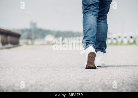 Close up Frau tragen Jean und weiße Sneaker vorwärts zu Fuß auf der Autobahn unterwegs in sonniger Tag, allein reisen oder Alleinreisende Konzept. Stockfoto