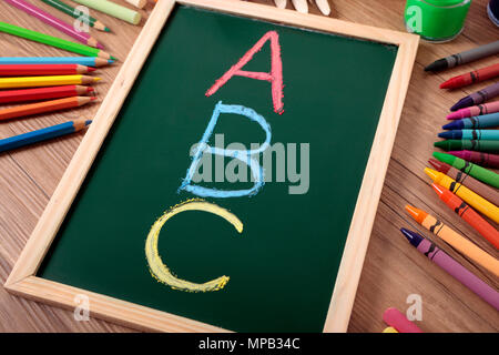 ABC in Farbe Kreide auf einer kleinen elementaren Tafel mit verschiedenen Farben, Kreiden und Stifte auf der Schulbank geschrieben. Stockfoto