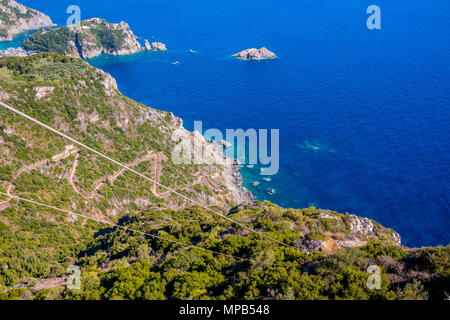 Serpentinenstraße in Berge mit Wald bedeckt. Herrliche Aussicht von Drohne, Insel Korfu, Griechenland. Das klare blaue Wasser. Luftaufnahme. Tolle Aussicht auf die Bucht von Palaiokastritsa Ionische Meer. Stockfoto