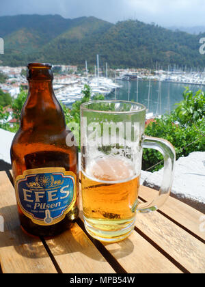 Ein Glas Efes Pilsen Bier mit Marmaris Marina im Hintergrund Stockfoto