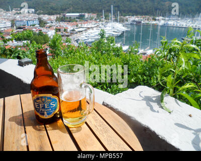 Ein Glas Efes Pilsen Bier mit Marmaris Marina im Hintergrund Stockfoto