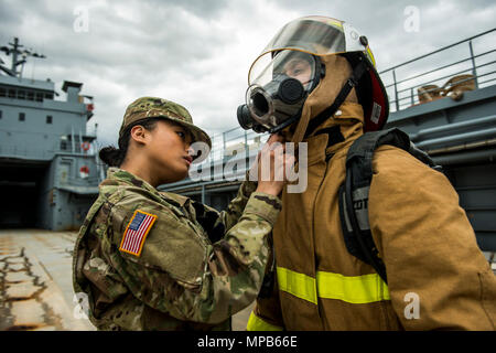 Spc. Angelina Utanes, ein US Army Reserve watercraft operator Soldat mit dem 949Th Transportation Company, unterstützt Spc. Huy Dinh mit eine Brandbekämpfung Anzug und Maske, für eine Reihe von Porträts und Bilder, die Ihre militärische Besetzung Spezialität während eines Stockfoto