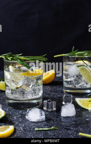 Alkoholisches Getränk Gin Tonic Cocktail mit Zitrone, Rosmarin und Eis auf Tisch aus Stein. Stockfoto
