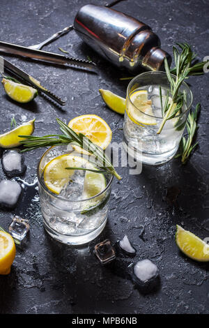 Alkoholisches Getränk Gin Tonic Cocktail mit Zitrone, Rosmarin und Eis auf Tisch aus Stein. Stockfoto