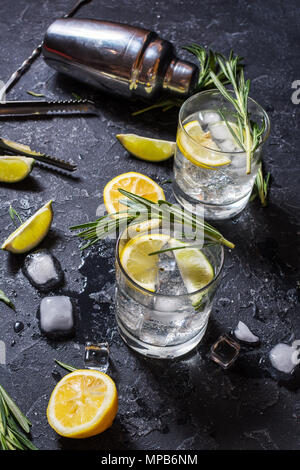 Alkoholisches Getränk Gin Tonic Cocktail mit Zitrone, Rosmarin und Eis auf Tisch aus Stein. Stockfoto