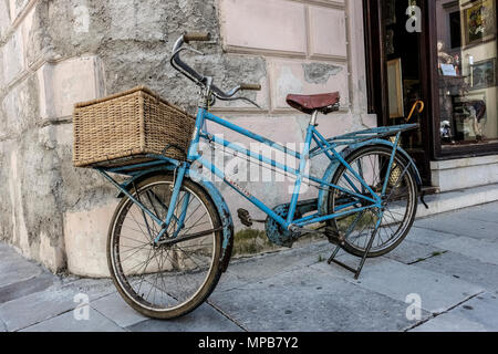 Hellblaues altes Fahrrad mit Lieferkorb, vor einem Laden geparkt. Görz, Italien, Europa, Europäische Union, EU. Stockfoto