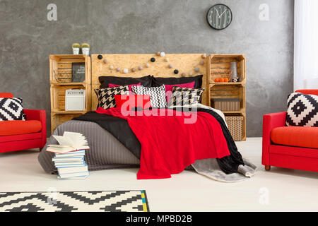 Graue Zimmer mit Doppelbett mit Kopfteil aus Holz. Rot komfortable Sessel und Holzfachböden in geräumigen Schlafzimmer Stockfoto