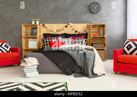 Geräumiges Schlafzimmer in Grau mit Doppelbett, DIY verwöhnt, Muster Details und zwei, rote Sessel Stockfoto