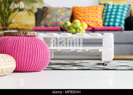 Interieur mit rosa Pouf, bunten Kissen, grau Couch, DIY-Tabelle Stockfoto