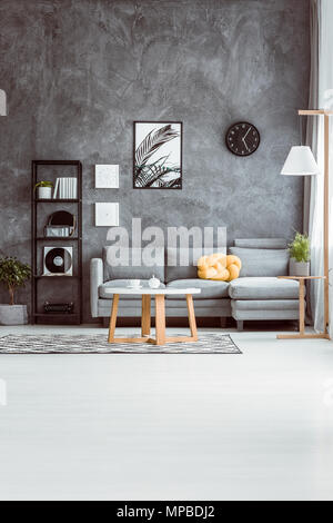 Geräumiges Wohnzimmer mit Tisch auf dem Teppich im skandinavischen Stil und graue Sofa gegen die Betonwand Stockfoto