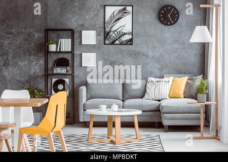 Multifunktionalen Wohnzimmer mit Esstisch und Anlage auf hölzernen Schemel in der Nähe von grau Couch mit Kissen gesetzt Stockfoto