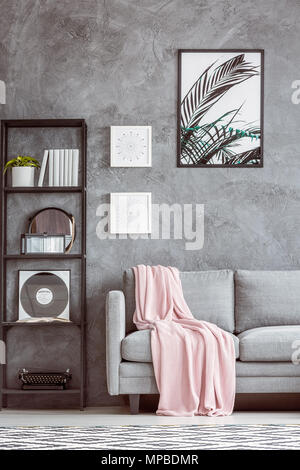 Die Schreibmaschine und Vinyl im Regal neben grau Sofa mit rosa Bettdecke gegen Betonmauer mit Poster Stockfoto