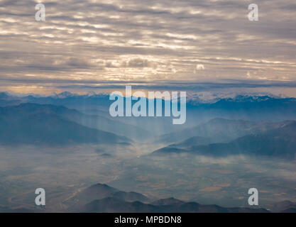 Blick aus dem Flugzeug Fenster fliegen südlich von Santiago, Chile mit Anden Berggipfel und Wolkenschichten von Wellen von Licht auf gebrochen Stockfoto
