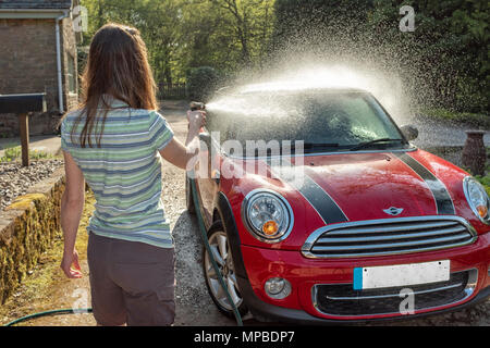 Eine Frau in den Vierzigern waschen Ihr Auto in der Sonne. Stockfoto