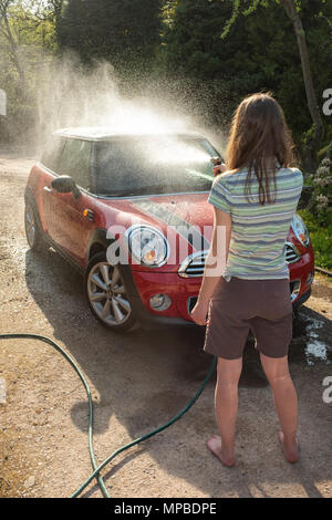 Eine Frau in den Vierzigern waschen Ihr Auto in der Sonne. Stockfoto