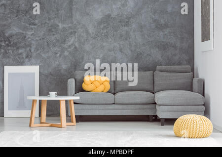 Gelbe pouf vor Grauen Sofa gegen Beton Wand im Wohnzimmer mit Tisch Stockfoto