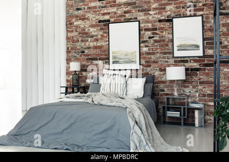 Bettdecke lag auf einem Kingsize-Bett mit grauem Deckel steht in einem Raum mit gerahmten Poster Stockfoto
