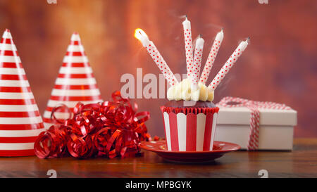 Geburtstag Cupcake mit Geschenk und Party Dekorationen gegen eine rustikale Holz Hintergrund, Kerzen ausblasen. Stockfoto