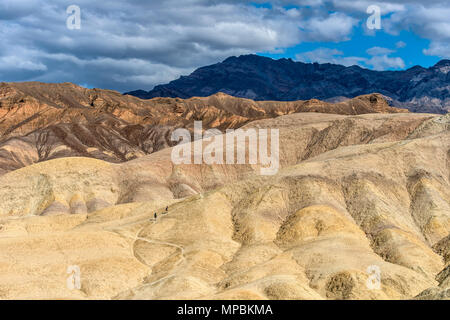 Wandern in der Wüste - Touristen wandern auf steilen Hügeln, als dunkle Feder vorbeiziehenden Wolken Overhead, in den Badlands von Death Valley National Park, USA. Stockfoto