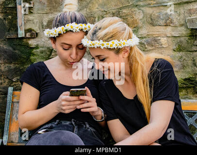 Zwei Mädchen im Teenager-Alter mit Blumengirlanden teilen einen Moment auf Ihrem Telefon in Sirince, Türkei Stockfoto