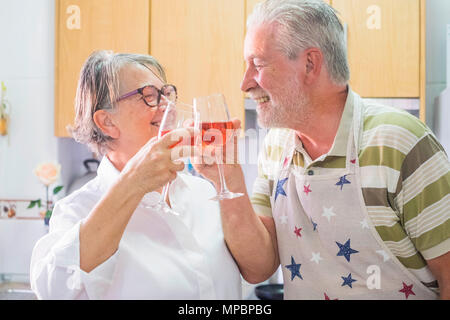 Älterer Mann und ältere Frau mit weißen Haaren Erwachsene in somne Spaß lächelnd in die Küche zu Hause trinken Rotwein. Stockfoto