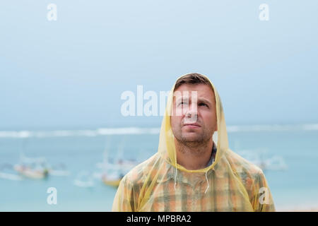 Kaukasische Mann stand in der Nähe von Meer am Strand Regenmantel tragen. Stockfoto