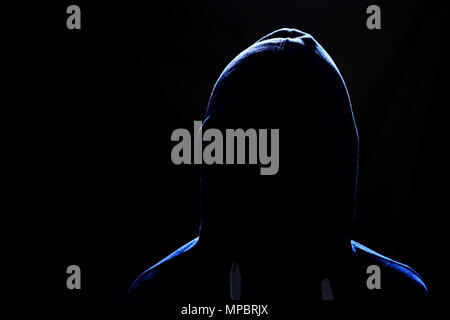 Gesichtslosen menschlichen Figur in einer Haube auf einem schwarzen Hintergrund. Das Konzept der Cyberkriminalität, Diebstahl im Netz. Eine gefährliche, finstere Person. Stockfoto