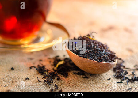 Trocken schwarze Teeblätter in einem Löffel aus Holz und eine Tasse duftenden Tee im Hintergrund. Kaffee Schweißen Stockfoto