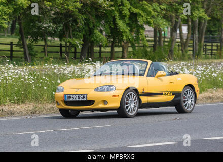 Gelbe Mazda MX-5 Arizona cabrio Sportwagen von 2002, mit der Oberseite nach unten auf eine britische Straße an einem heißen Tag in Großbritannien. Mazda soft top Auto. Stockfoto