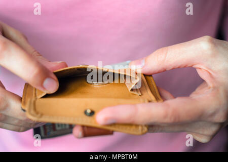 Eine Münze in eine leere Brieftasche in der Hand der Frau. Ein Mädchen in einem rosa Pullover hält eine Geldbörse mit der letzten Münze. Stockfoto