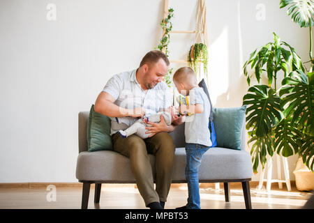 Foto der jungen Vater mit zwei Söhnen sitzt auf einem Sofa Stockfoto