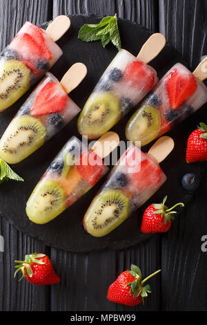 Obst Eis auf einem Stick von Erdbeeren, Kiwi und Blaubeeren mit Minze close-up auf einem Teller auf den Tisch. Vertikal oben Ansicht von oben Stockfoto