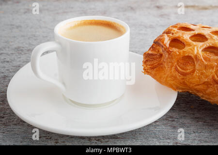 Eine duftende Tasse frisch gebrühten Kaffee und ein Croissant auf einem hölzernen Hintergrund Stockfoto