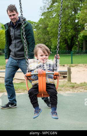 Vater seinen 18 Monate alten Sohn auf einem Spielplatz Schaukel drücken Stockfoto