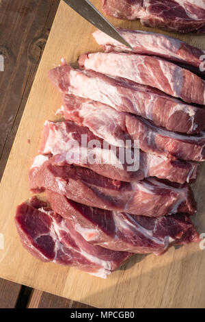 Raw leckere Scheiben schneiden Schweinefleisch Steaks zu tun. Schweinefleisch auf dem Holz boardbackground mit Messer Stockfoto