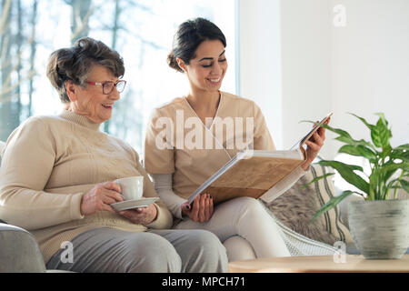 Lächelnd professionelle Hausmeister zeigt eine Familie Album auf eine ältere Frau in einem Wohnzimmer zu Hause Stockfoto