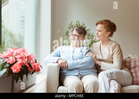 Eine ältere Frau mit einem medizinischen Support Professional sitzen auf einem Sofa während des Wartens auf einen geriatrischen Facharzt Termin in einem privaten medizinischen Stockfoto
