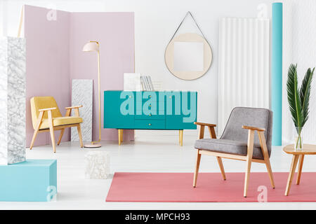 Blätter auf hölzernen Tisch neben einem grauen Sessel auf rosa Teppich im Innenraum mit Green cabinet Stockfoto