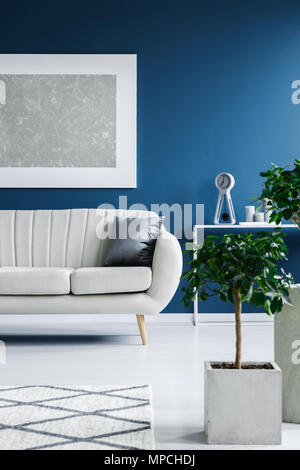 Pflanzen in Töpfen, Malerei auf einer blauen Wand und elegantes Sofa im Wohnzimmer Innenraum Stockfoto