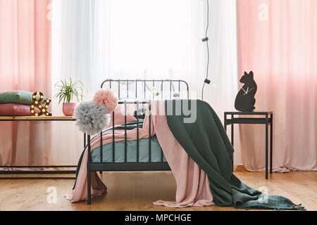 Vorderansicht eines Einzelbett mit Pompons, Wolldecken und pinkfarbenen Vorhängen in einem Schlafzimmer Innenraum Stockfoto