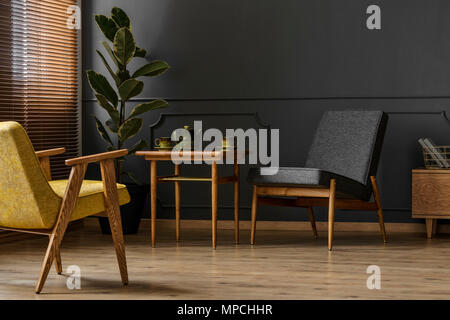 Einfache, dunkle retro Wohnzimmer Innenraumkonzept mit zwei Stühle, Hocker, Teekanne und Anlage Stockfoto