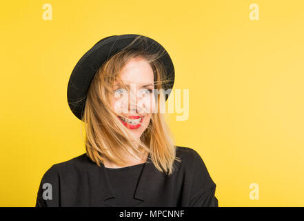 Portrait einer jungen schönen Frau mit schwarzem Hut im Studio auf einem gelben Hintergrund. Stockfoto