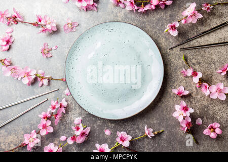 Essstäbchen und Sakura Filialen auf grauem Stein Hintergrund. Japanisches Essen Konzept. Ansicht von oben, kopieren Raum Stockfoto