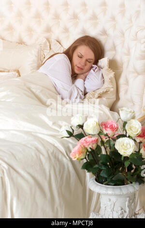 Romantik. Schöne schlafende Frau in Weiß mit roten Rosen Stockfoto