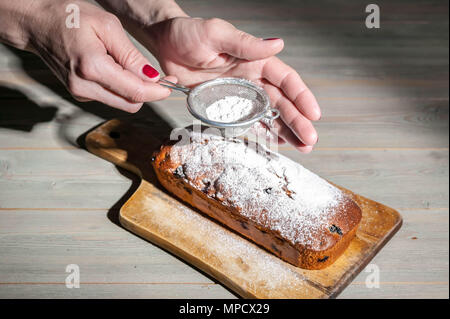 Frauenhände, mit Staubzucker bestreuen hausgemachten Blueberry Muffin Stockfoto